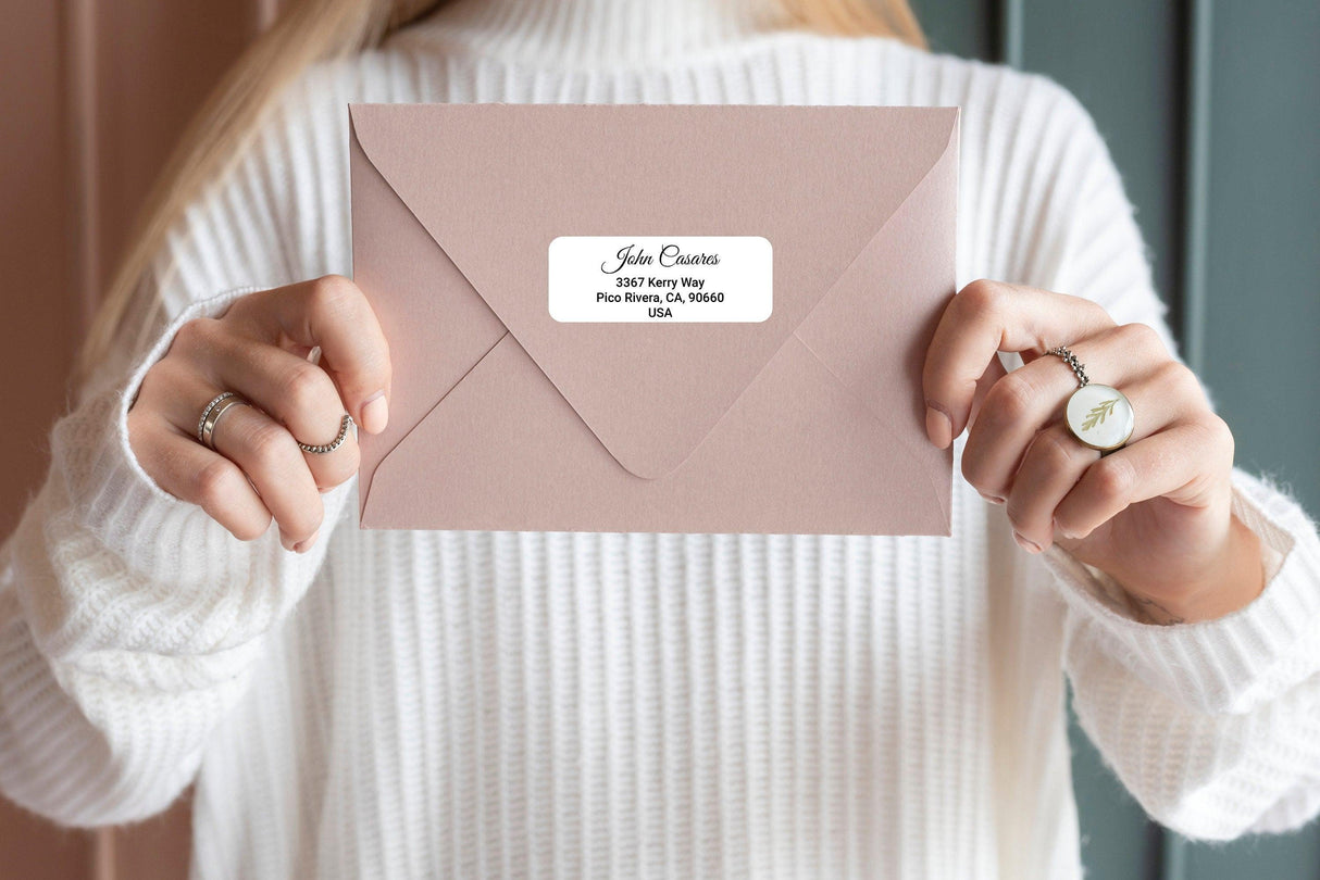 Personalized return address label on a pink envelope held by a person, showcasing custom mailing stickers.