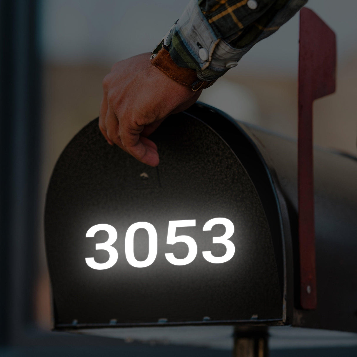 Hand placing reflective address decal '3053' on mailbox for easy visibility in low light conditions.