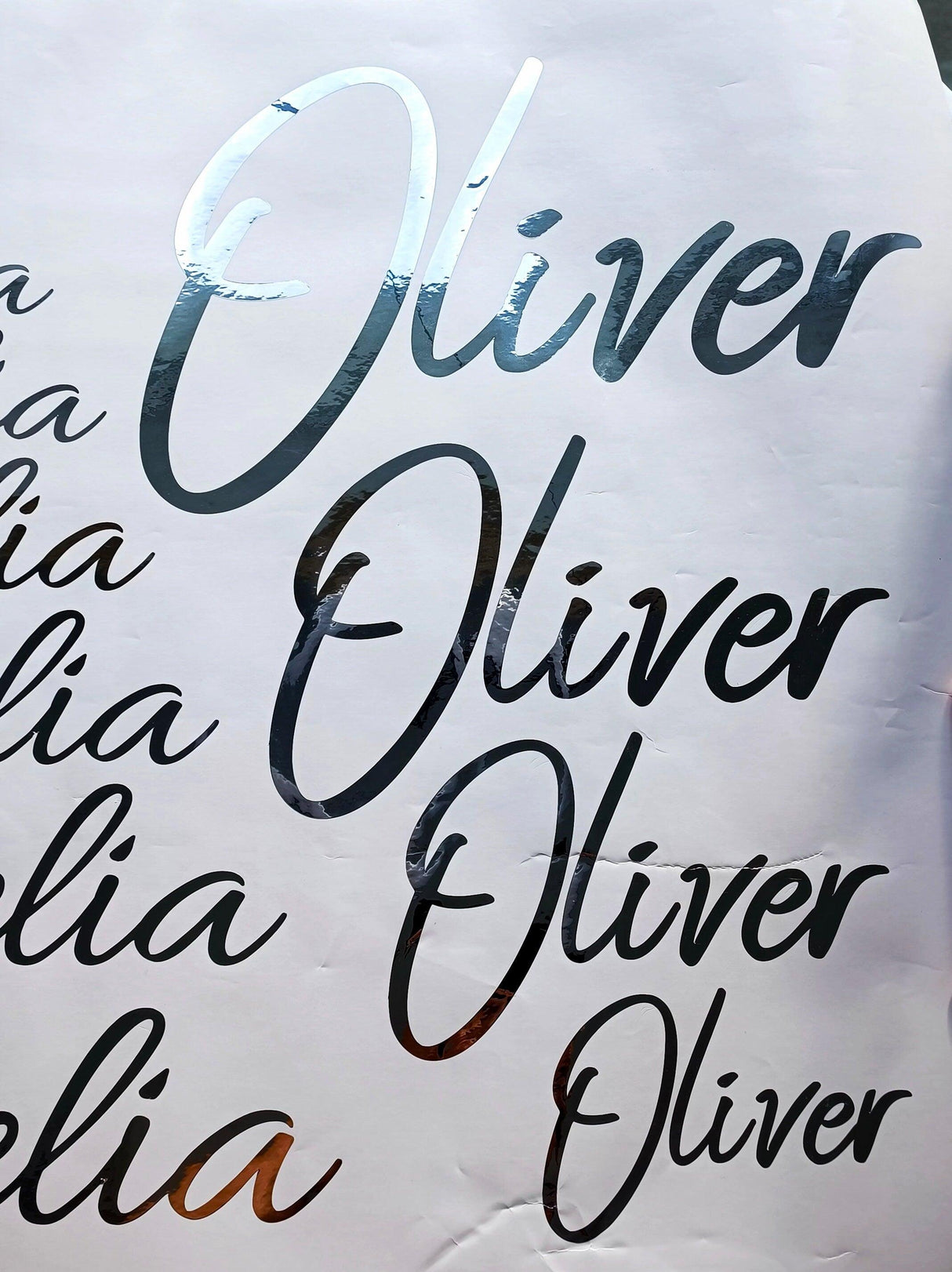 Close-up of personalized vinyl name stickers with silver chrome finish featuring the name 'Oliver' in various styles.