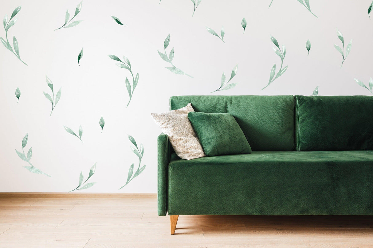 Leaf Wall Decor Stickers in green on a white wall behind a modern green sofa with decorative cushions.