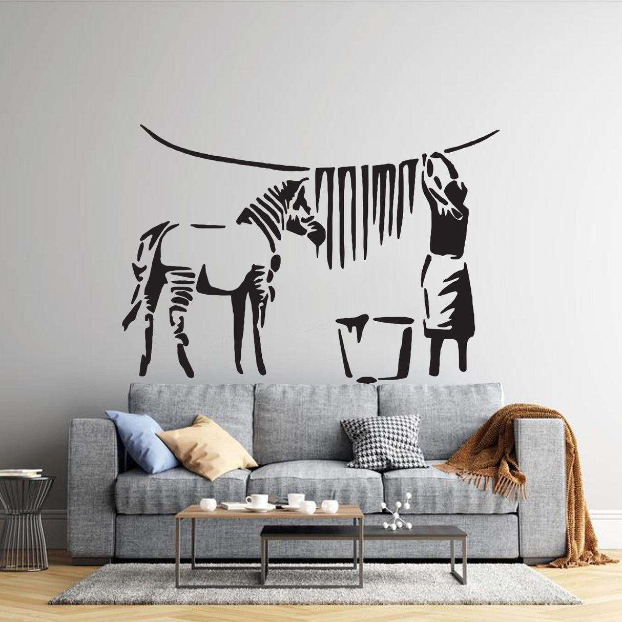Banksy zebra stripes wall decal on a living room wall above a modern gray sofa, adding urban street art vibes.