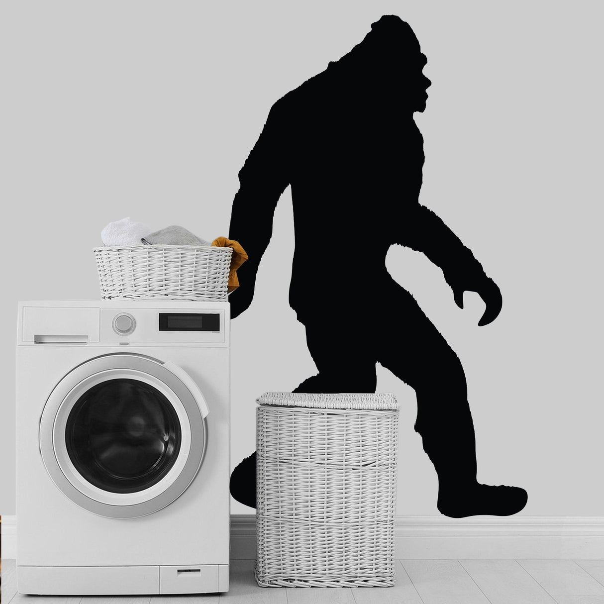 Big Foot Sasquatch vinyl wall decal on a gray wall near a washing machine and laundry baskets.