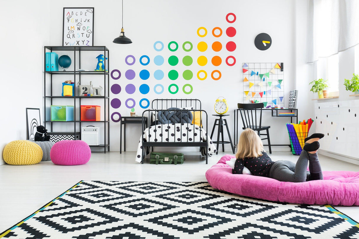 Colorful rainbow circle wall decals in a modern room with a girl lounging on a pink bean bag chair.