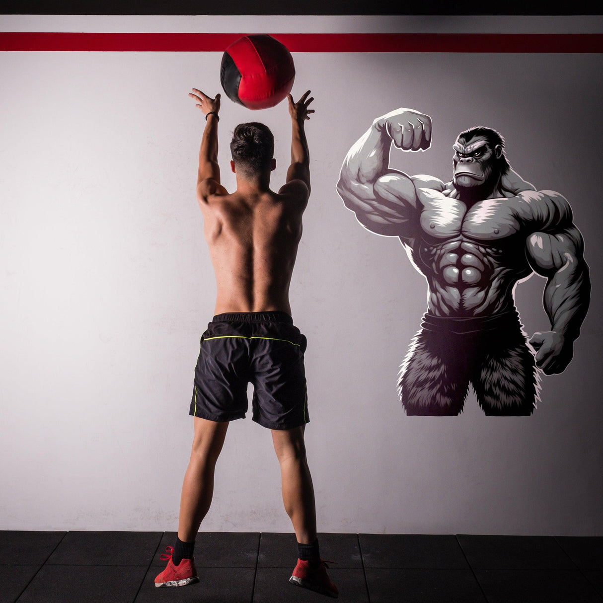 A fit person performing a workout with a medicine ball next to a muscled gorilla gym wall decal.