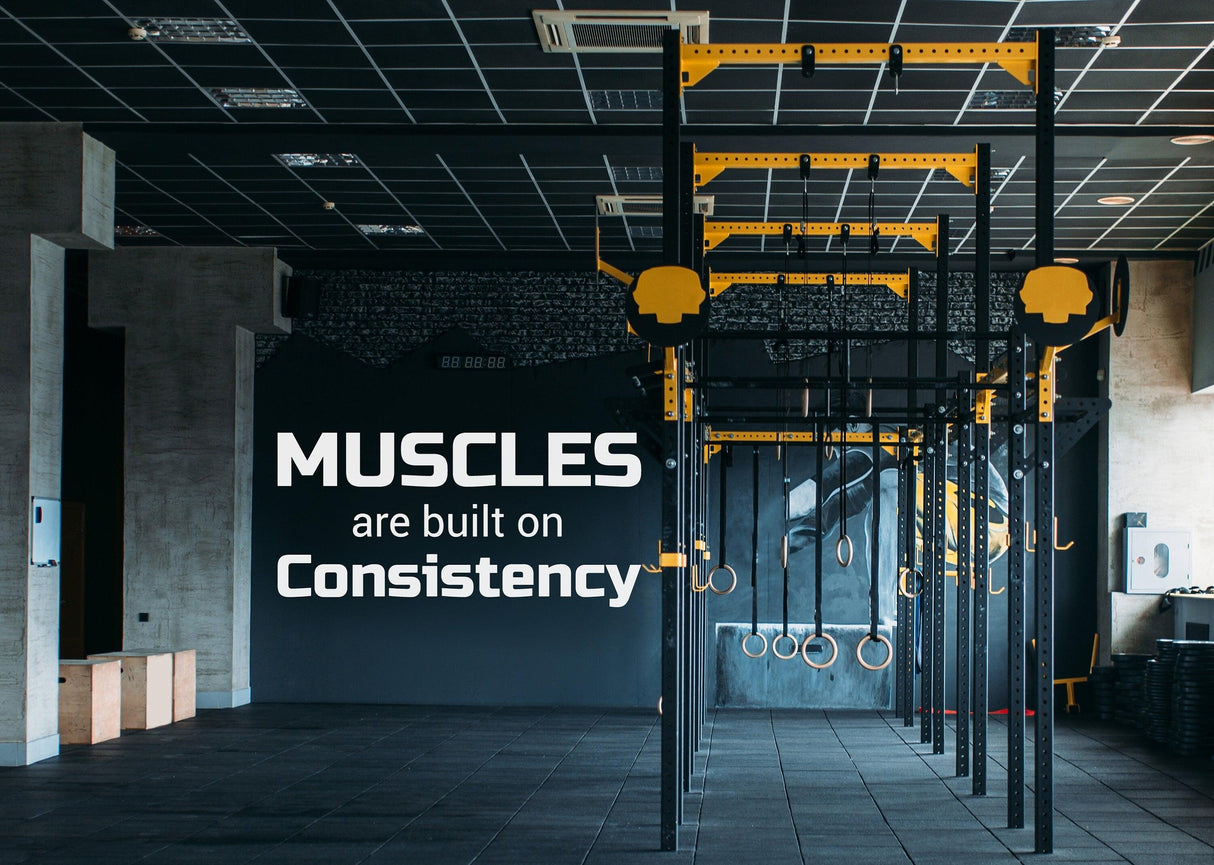 Fitness motivation wall with quote: 'Muscles are built on Consistency' in a modern gym.