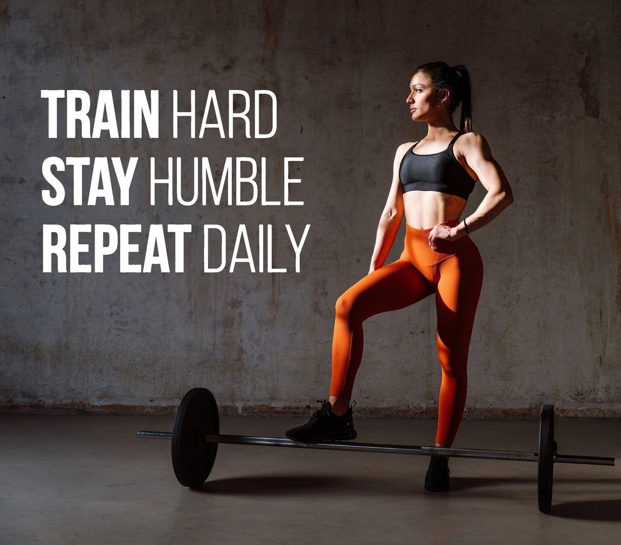 Fitness enthusiast showcasing motivational quote for gym: Train Hard, Stay Humble, Repeat Daily.