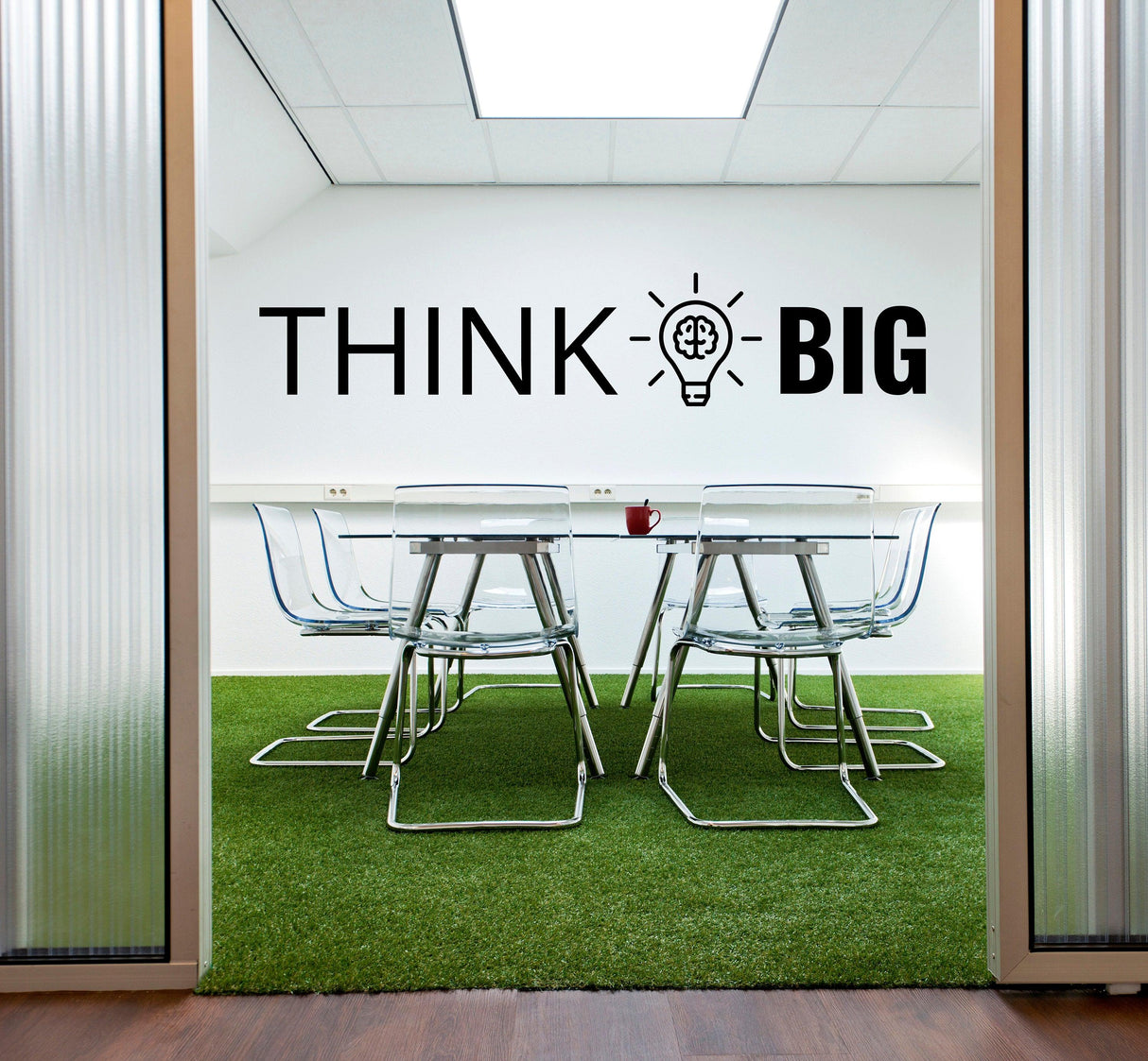 Modern office with 'THINK BIG' motivational wall decal and glass conference table on grassy carpet.