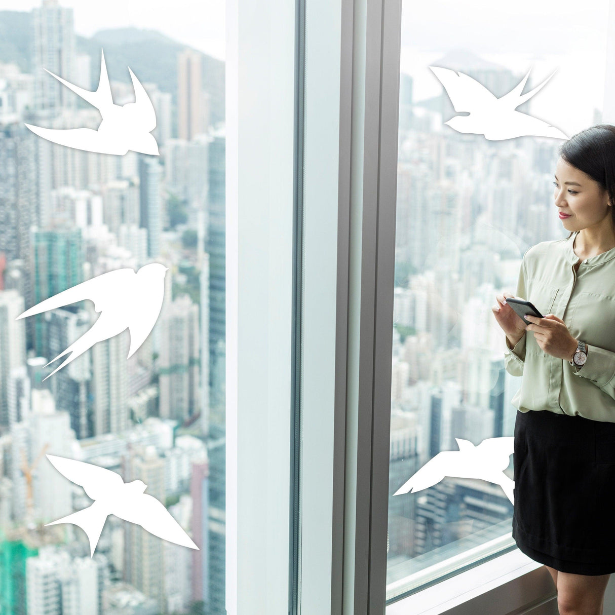 Woman standing by a window with anti-collision bird decals applied to prevent bird strikes.