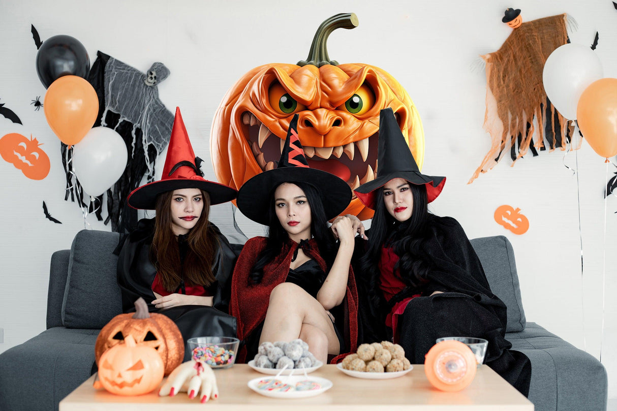 Three witches in stylish costumes enjoying Halloween decorations with a spooky pumpkin backdrop and festive treats.
