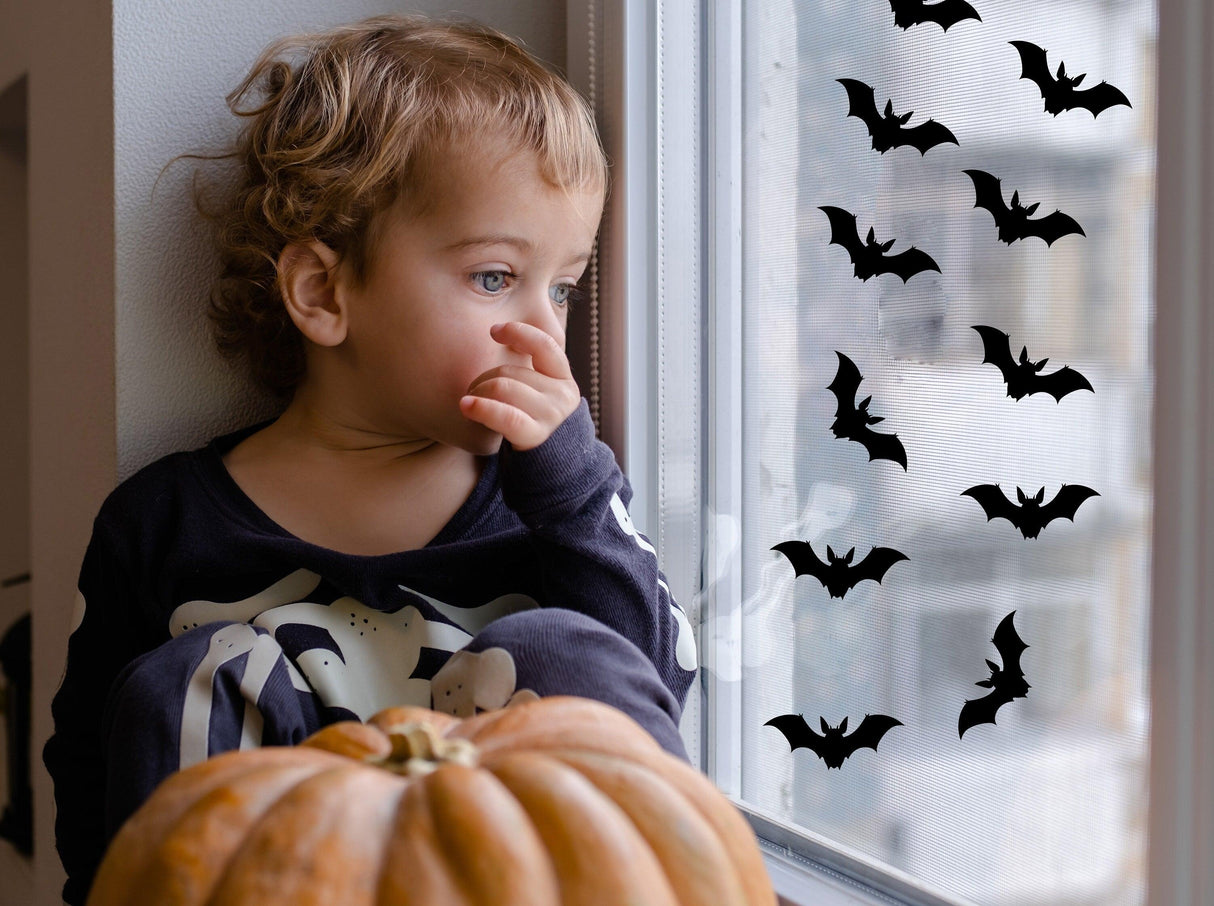 Child by a window with Halloween bat decals, featuring a pumpkin for festive Halloween decorations.