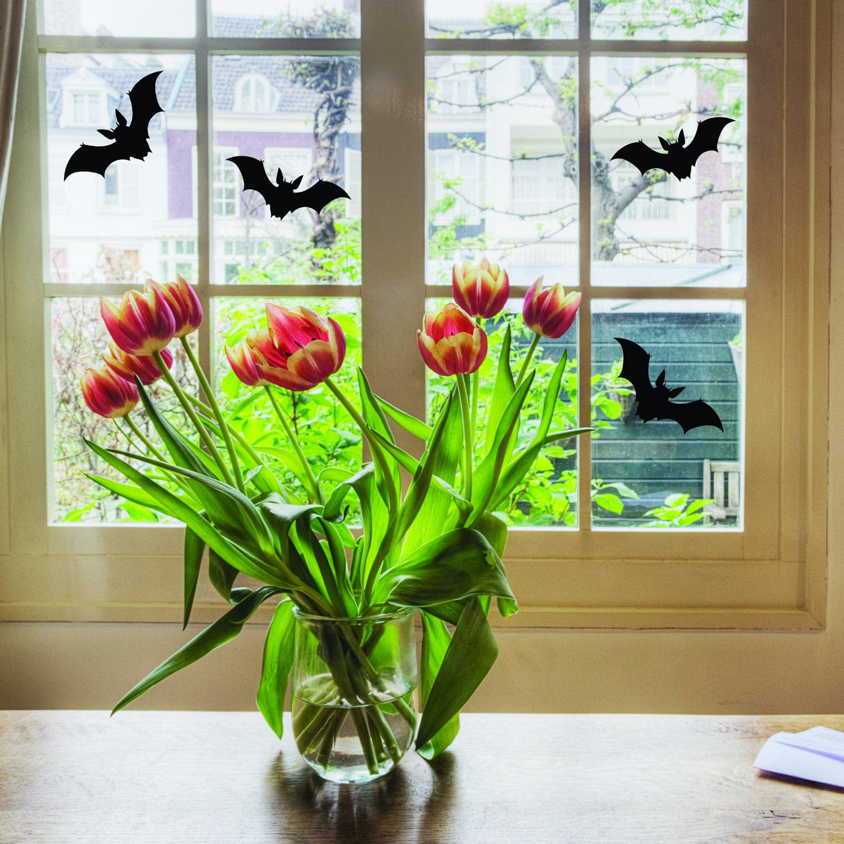 Halloween bats window decals on a home window with tulips, perfect for October 31st decorations.