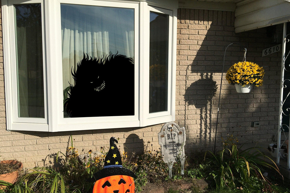 Halloween monster window decal creating a spooky silhouette effect outside a house with festive decorations.