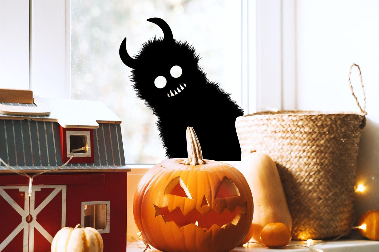 Halloween Haunting Window Art featuring a monster shadow sticker by a carved pumpkin on a windowsill.