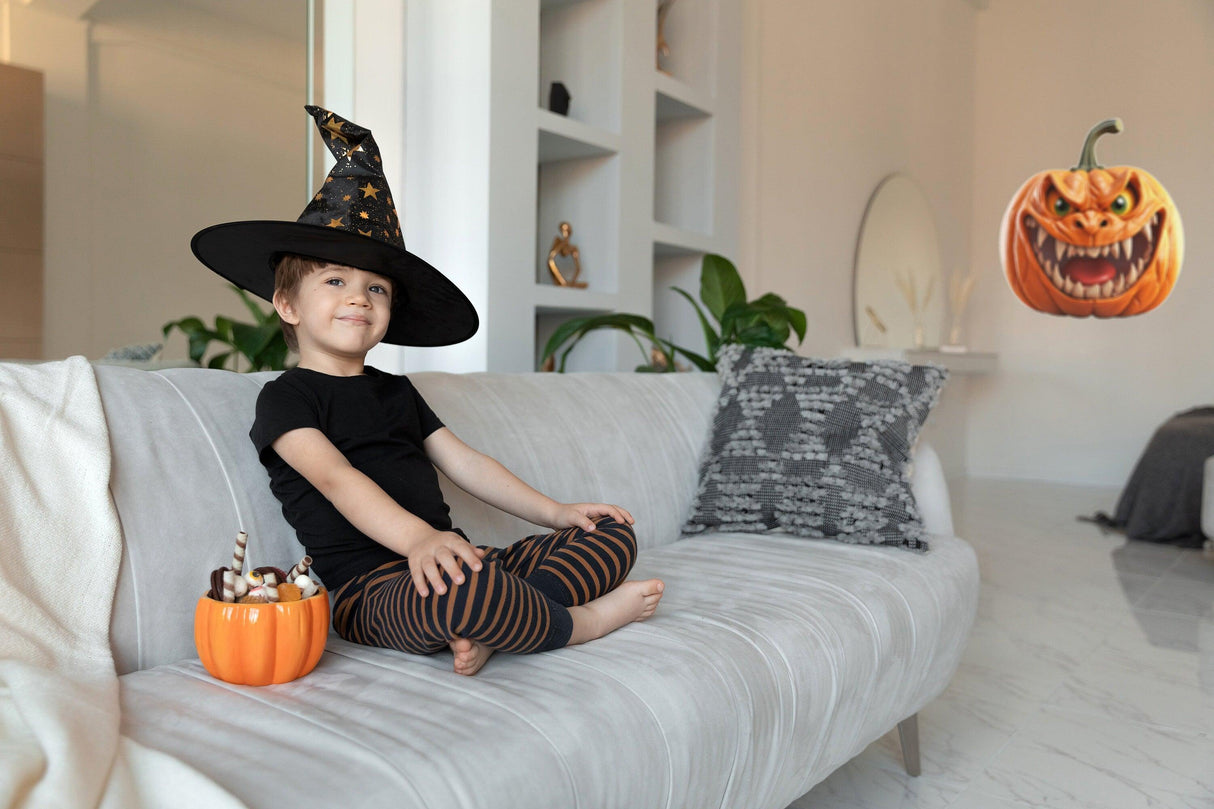 Child in witch hat sitting on couch with Halloween candy in pumpkin bucket and evil laughing pumpkin decal in background.