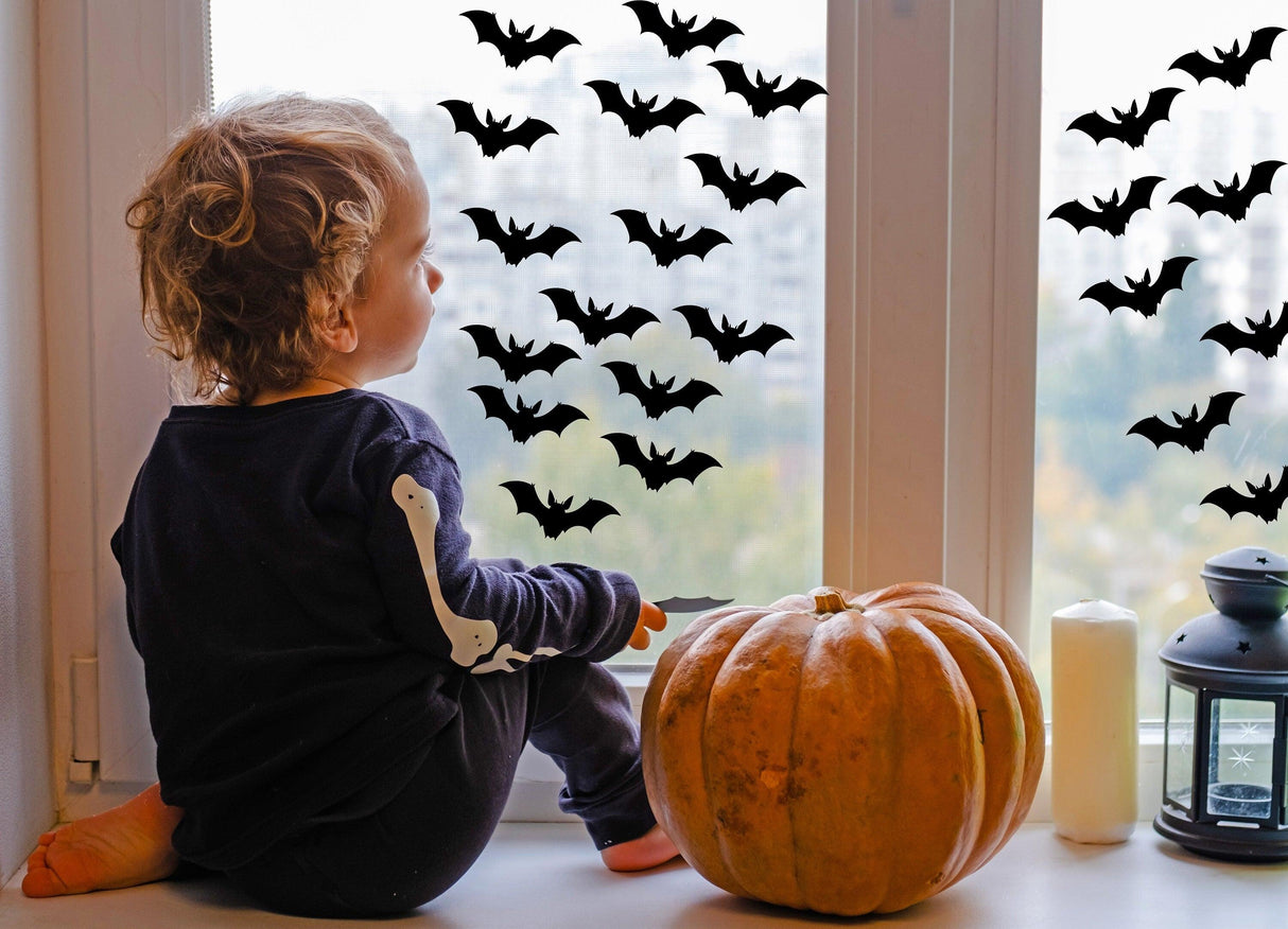 Child looking out the window decorated with Halloween bats decals and a pumpkin beside them.