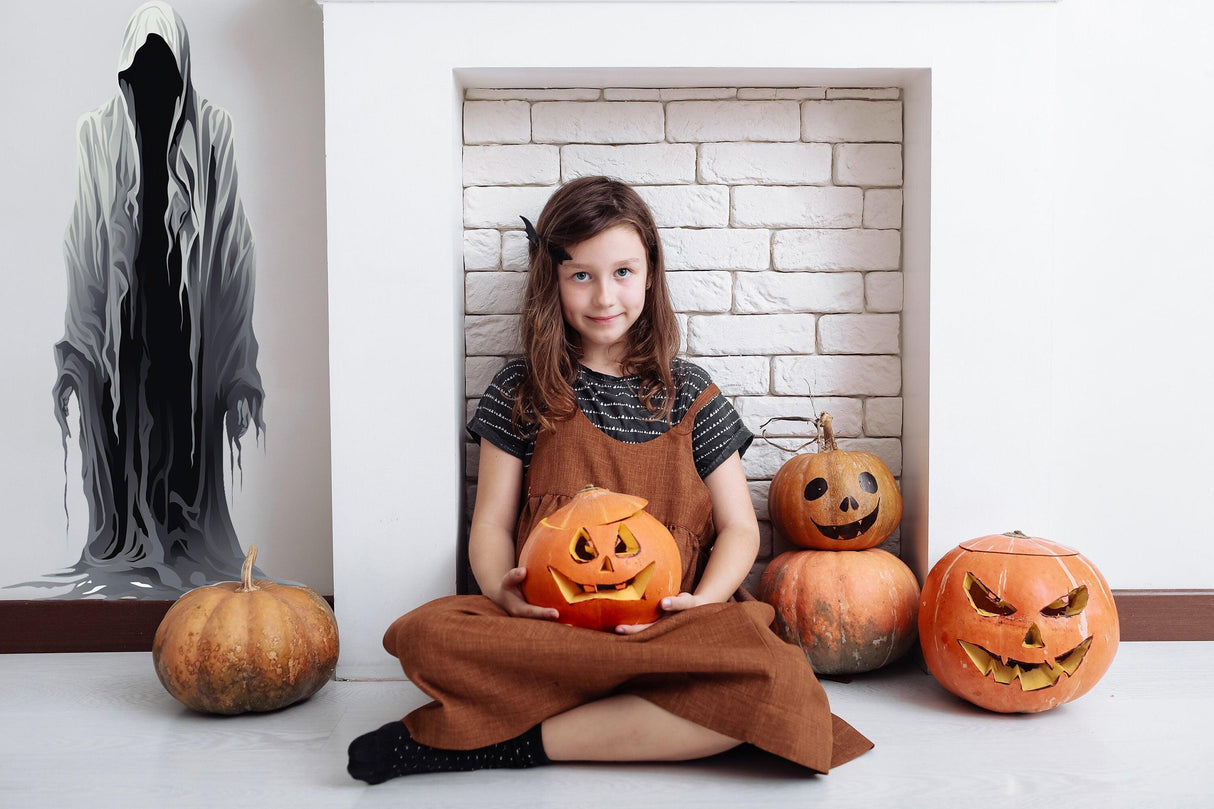 Child sitting with Halloween pumpkins, spooky wall decal, creating a festive haunted atmosphere.
