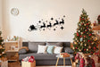 Santa sleigh with reindeer silhouette decal above cozy sofa and Christmas trees for festive home decor.