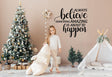 Child standing by Christmas tree with vinyl sticker saying 'Always Believe Something Amazing is About to Happen'.