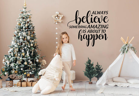 Child standing by Christmas tree with vinyl sticker saying 'Always Believe Something Amazing is About to Happen'.