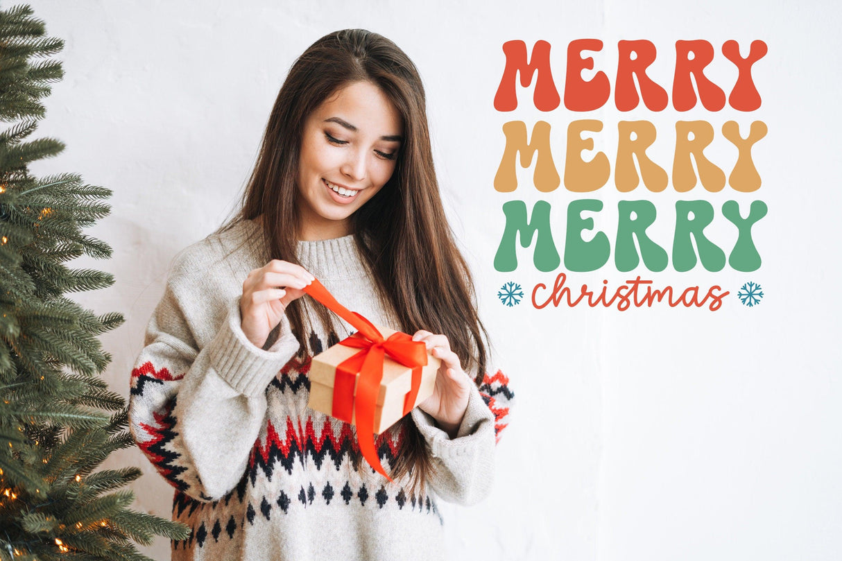 Smiling woman in sweater holding a gift with a colorful 'Merry Merry Merry Christmas' wall sticker in background.