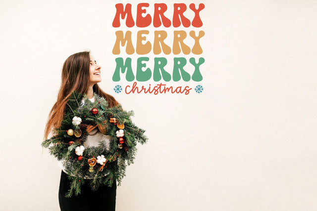 Woman holding a festive wreath with colorful 'Merry Merry Merry Christmas' wall decal sign.
