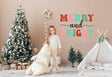 Child holding a stuffed animal near a Christmas tree with 'Merry and Bright' wall decal for festive decor.