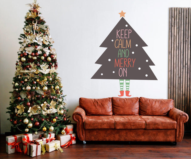 Whimsical Christmas tree with legs wall sticker saying 'Keep Calm and Merry On' above a cozy sofa with a decorated Christmas tree.