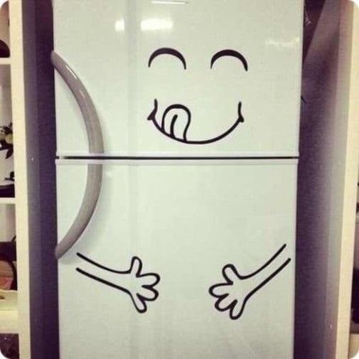 Cute vinyl sticker on white fridge showcasing a smiling face and playful hands, adding humor to kitchen decor.