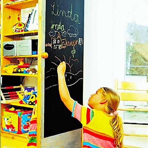 Child drawing on a black chalkboard wall decal, showcasing creativity in a colorful kitchen environment.