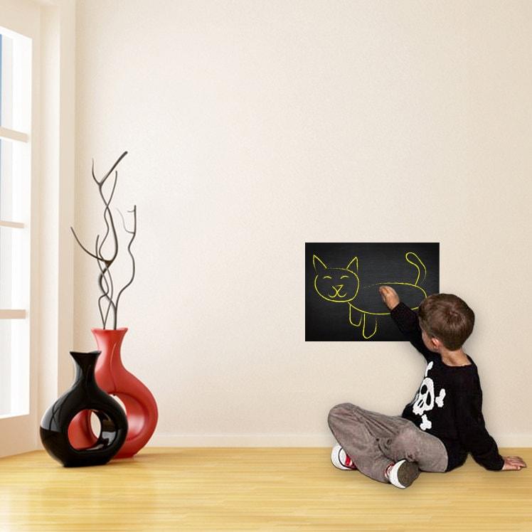 Child drawing a cat on a chalkboard wall sticker in a stylish living room with modern decor.