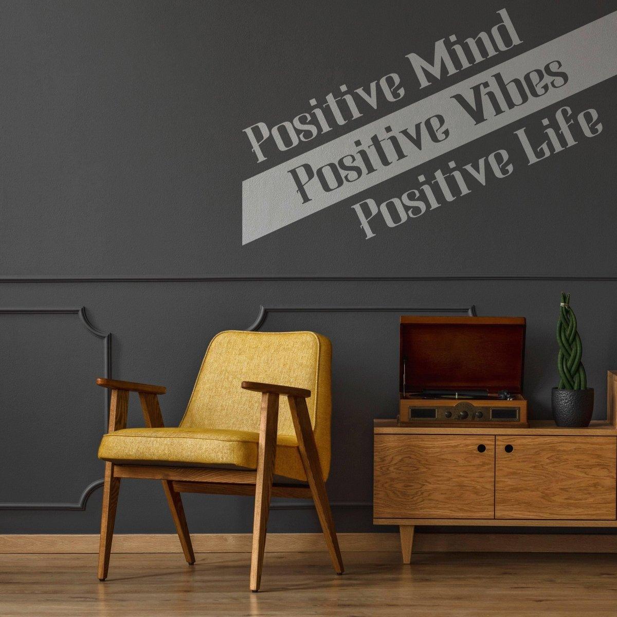 Motivational vinyl decal on dark wall reading 'Positive Mind Positive Vibes Positive Life' above a yellow chair.