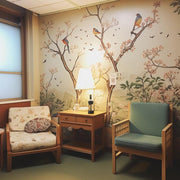 Cozy seating area with floral wallpaper and birds, featuring two chairs and a lamp.