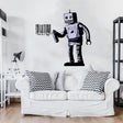Wall decal of a retro robot spray painting a barcode on a white wall above a modern white couch with black and white zigzag pillows in a minimalist living space.
