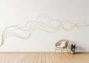A large, abstract gold swirl line decal flows across a white wall in a minimal modern interior.