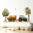 A playful wall decal featuring a green farm tractor pulling a trailer with hay bales between two trees, placed in a child's room above a wooden floor with toy blocks and trucks scattered around.