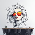 Wall decal of a woman with short wavy white hair and vivid orange reflective sunglasses in comic-style illustration, installed above a modern dining counter with black bar chairs.