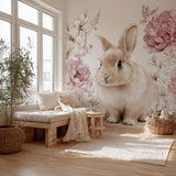 A cozy, sunlit nursery room with a giant wall decal of a fluffy light brown bunny surrounded by watercolor-style pink and white flowers, styled with natural wood furniture and soft boho textiles.