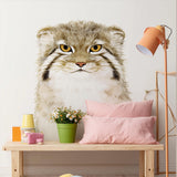 Illustrated vinyl wall decal of a Pallas’s cat (manul) with golden eyes and soft fur details, applied above a wooden bench with pink pillows in a cozy children’s room.
