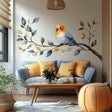 Vinyl wall decal of a soft watercolor-style bird sitting on a leafy branch, applied above a light sofa with yellow pillows in a cozy, sunlit living room.