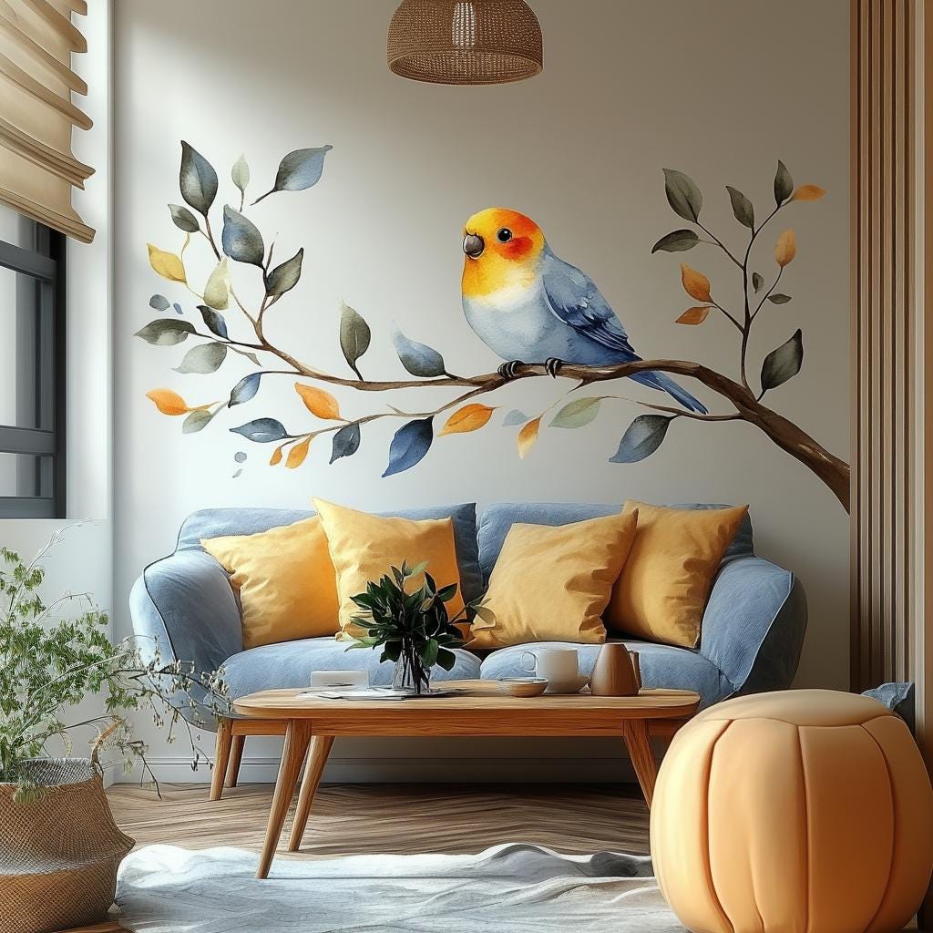 Vinyl wall decal of a soft watercolor-style bird sitting on a leafy branch, applied above a light sofa with yellow pillows in a cozy, sunlit living room.
