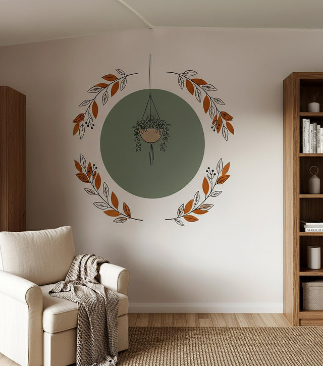 Vinyl wall decal featuring a hanging plant centered over a green circle, framed by terracotta and beige botanical branches. Applied above a beige armchair in a cozy modern living room with wooden furniture.