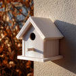 Light-colored 3D printed birdhouse with perch and removable roof made from matte PLA plastic, mounted on an exterior wall in soft natural sunlight.