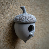 3D printed acorn-shaped birdhouse with round entrance and small cylindrical perch made of matte PLA plastic, mounted on a textured exterior wall.