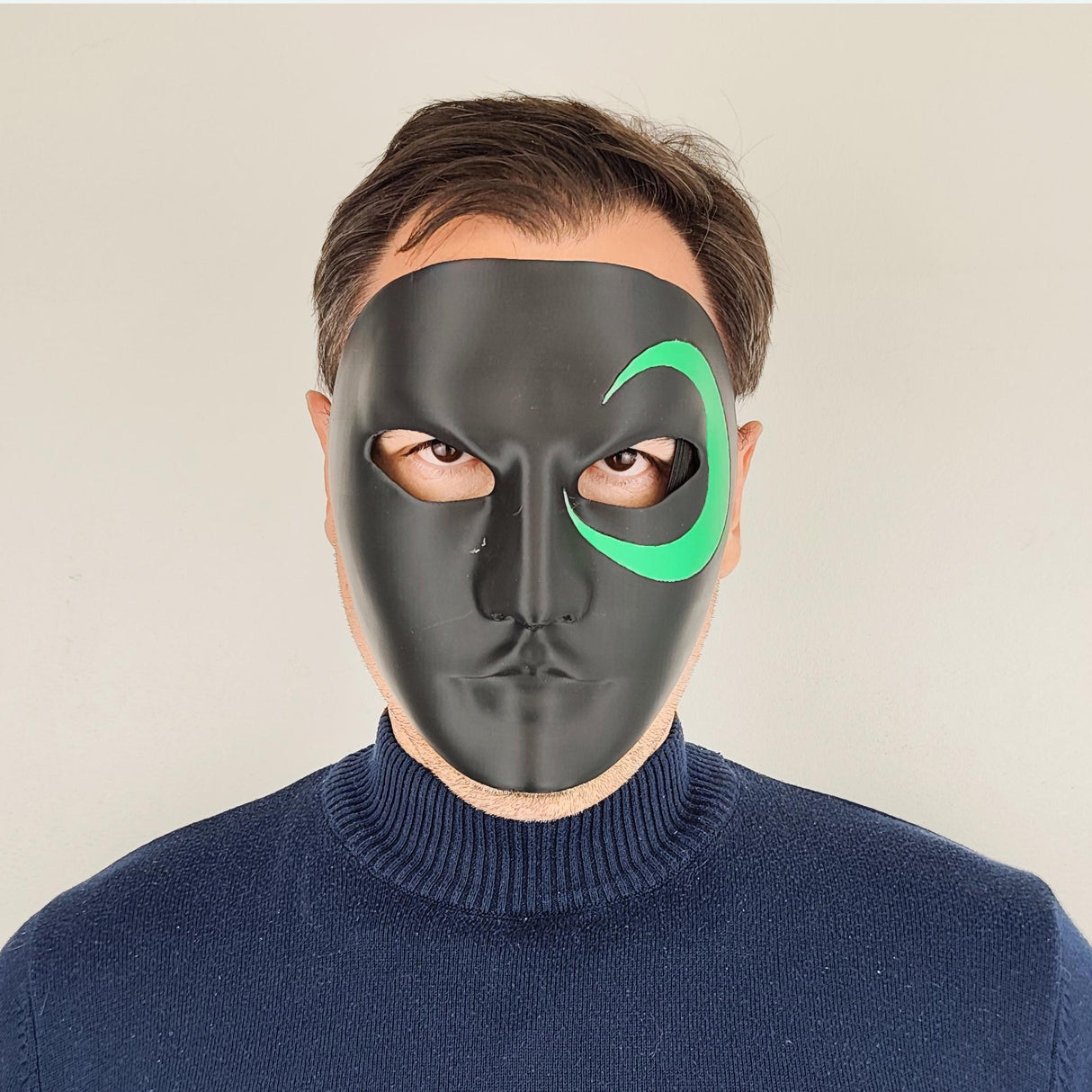Person wearing a black 3D-printed half-face mask with a green crescent design around one eye; photographed from various angles including front, side, and ¾ view, showing detail, shape, and fit of the mask.