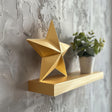 3D printed star-shaped wall shelf in matte gold finish with geometric design, styled with a small plant on a textured gray wall