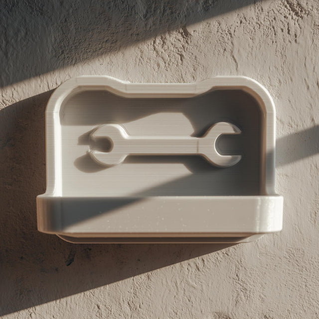 3D printed wall-mounted tool shelf with a shallow tray and embossed wrench icon on the back panel, matte light PLA finish, fixed on a textured workshop wall.