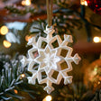 3D printed snowflake ornament made of matte PLA plastic hanging on a Christmas tree, minimalist modern holiday decoration.