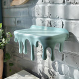 3D printed wall-mounted shelf with playful dripping “melting” design, matte pastel PLA surface, used as a small floating shelf on a brick wall