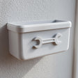 3D printed white wall-mounted organizer bin with an embossed wrench icon on the front, attached to a textured wall in a garage or utility room.
