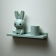 3D printed wall shelf with a slim back-edged ledge holding a rounded bunny character and a cylinder pot, mounted on a light-colored wall.